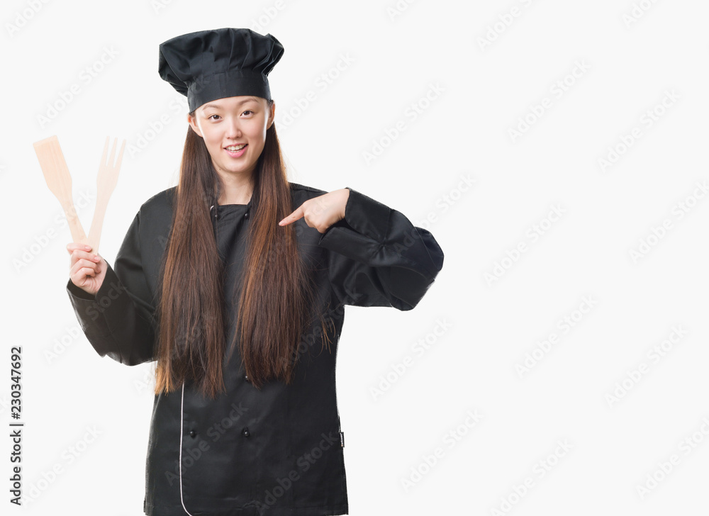 Young Chinese woman over isolated background wearing chef uniform with surprise face pointing finger to himself Young Chinese woman over isolated background wearing chef uniform with surprise face pointing finger to himself