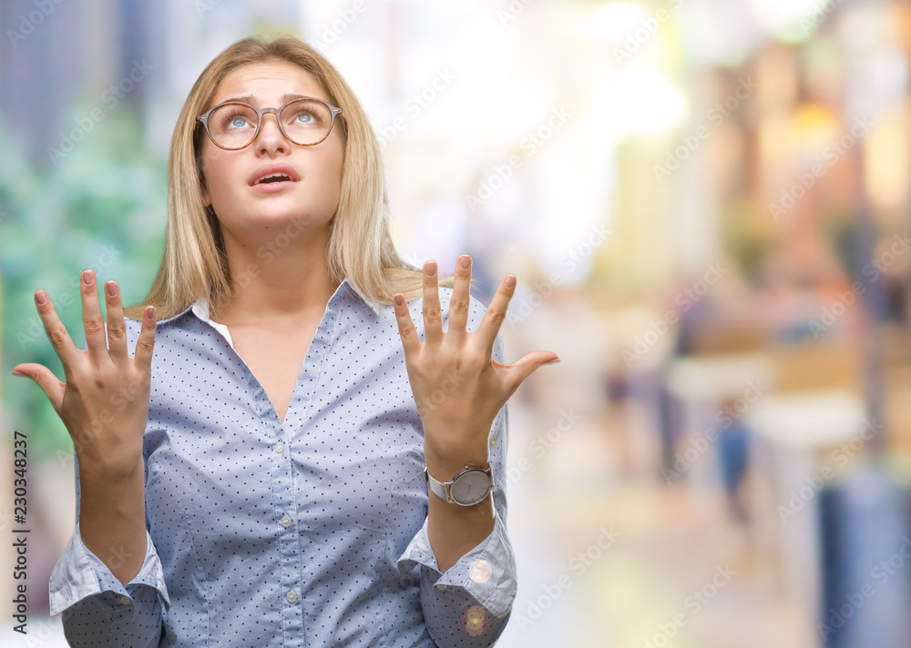 Young caucasian business woman wearing glasses over isolated background crazy and mad shouting and yelling with aggressive expression and arms raised. Frustration concept. Young caucasian business woman wearing glasses over isolated background crazy and mad shouting and yelling with aggressive expression and arms raised. Frustration concept.