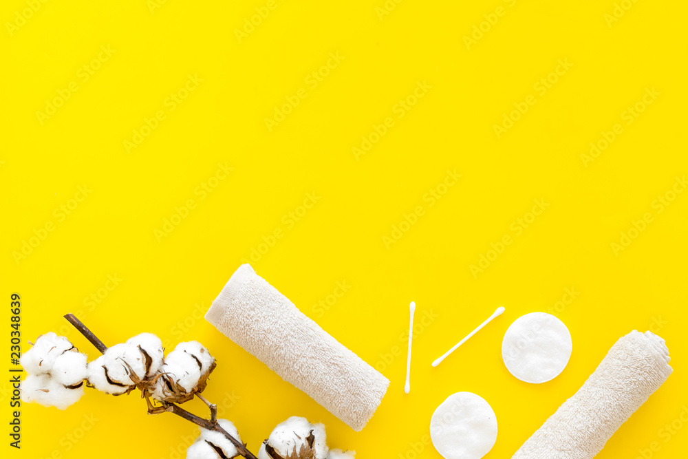 Fototapeta premium Products made of cotton. Bath accessories. Towels, cotton pads and swabs near dry cotton flowers on yellow background top view copy space