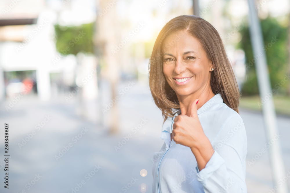 Beautiful middle age hispanic woman at the city street on a sunny day happy with big smile doing ok sign, thumb up with fingers, excellent sign Beautiful middle age hispanic woman at the city street on a sunny day happy with big smile doing ok sign, thumb up with fingers, excellent sign