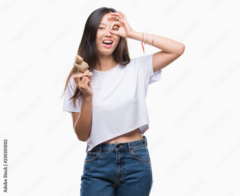 Young asian woman holding fresh organic over isolated background with happy face smiling doing ok sign with hand on eye looking through fingers Young asian woman holding fresh organic over isolated background with happy face smiling doing ok sign with hand on eye looking through fingers