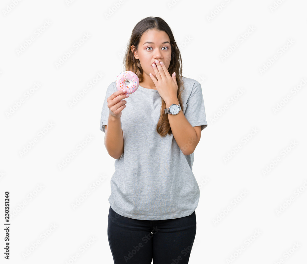 Young beautiful woman eating pink donut over isolated background cover mouth with hand shocked with shame for mistake, expression of fear, scared in silence, secret concept Young beautiful woman eating pink donut over isolated background cover mouth with hand shocked with shame for mistake, expression of fear, scared in silence, secret concept
