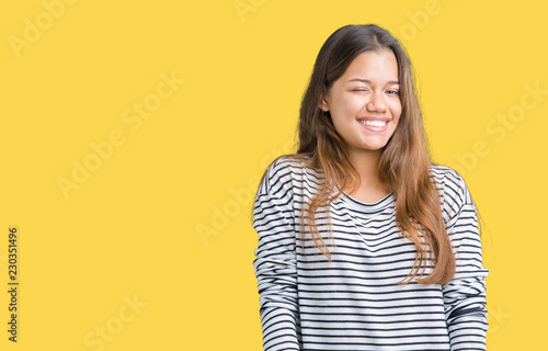Young beautiful brunette woman wearing stripes sweater over isolated background winking looking at the camera with sexy expression, cheerful and happy face. © Krakenimages.com
