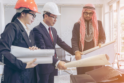Arabic or western business people speaking about investments while meeting or discussing with Partner Business teamwork trust partnership group of Asian business people or engineers with blueprint.