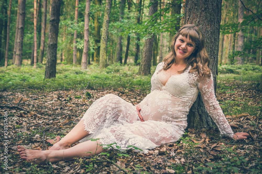Beautiful pregnant woman in white lace dress in forest Beautiful pregnant woman in white lace dress in forest