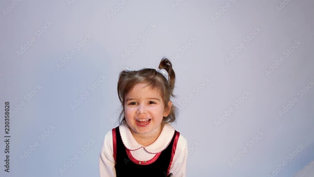 An adorable little girl with two pigtails stands in front of a plain backdrop with a blank expression staring at the camera. Her face suddenly lights up and she points to her cheek with a huge smile. An adorable little girl with two pigtails stands in front of a plain backdrop with a blank expression staring at the camera. Her face suddenly lights up and she points to her cheek with a huge smile.