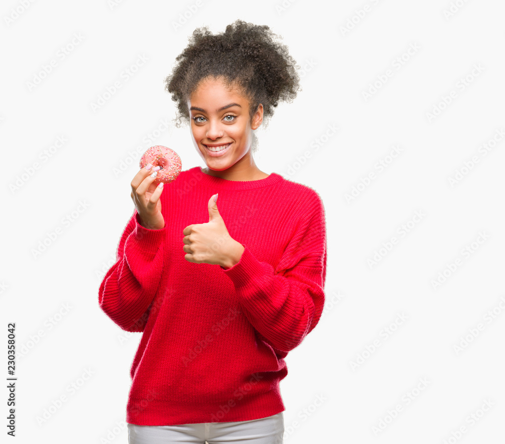 Young afro american woman eating donut over isolated background happy with big smile doing ok sign, thumb up with fingers, excellent sign Young afro american woman eating donut over isolated background happy with big smile doing ok sign, thumb up with fingers, excellent sign