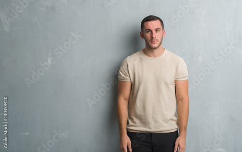 Young caucasian man over grey grunge wall with serious expression on face. Simple and natural looking at the camera. © Krakenimages.com