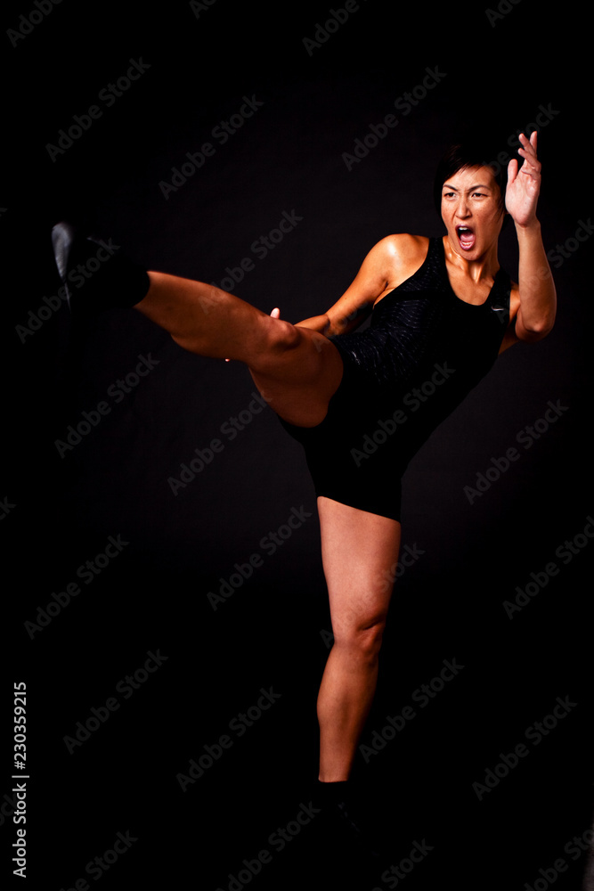 Asian woman kick boxing isolated on black.