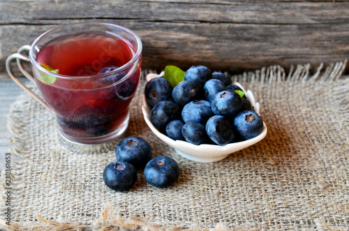 Blueberry tea in a glass cup and fresh blueberries on a burlap cloth on wooden background.Natural herbal beverage.Selective focus.