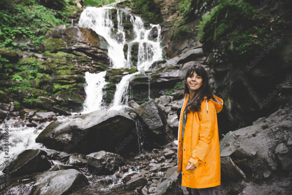 Naklejka premium woman standing in yellow raincoat and looking at waterfall