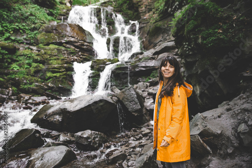 woman standing in yellow raincoat and looking at waterfall