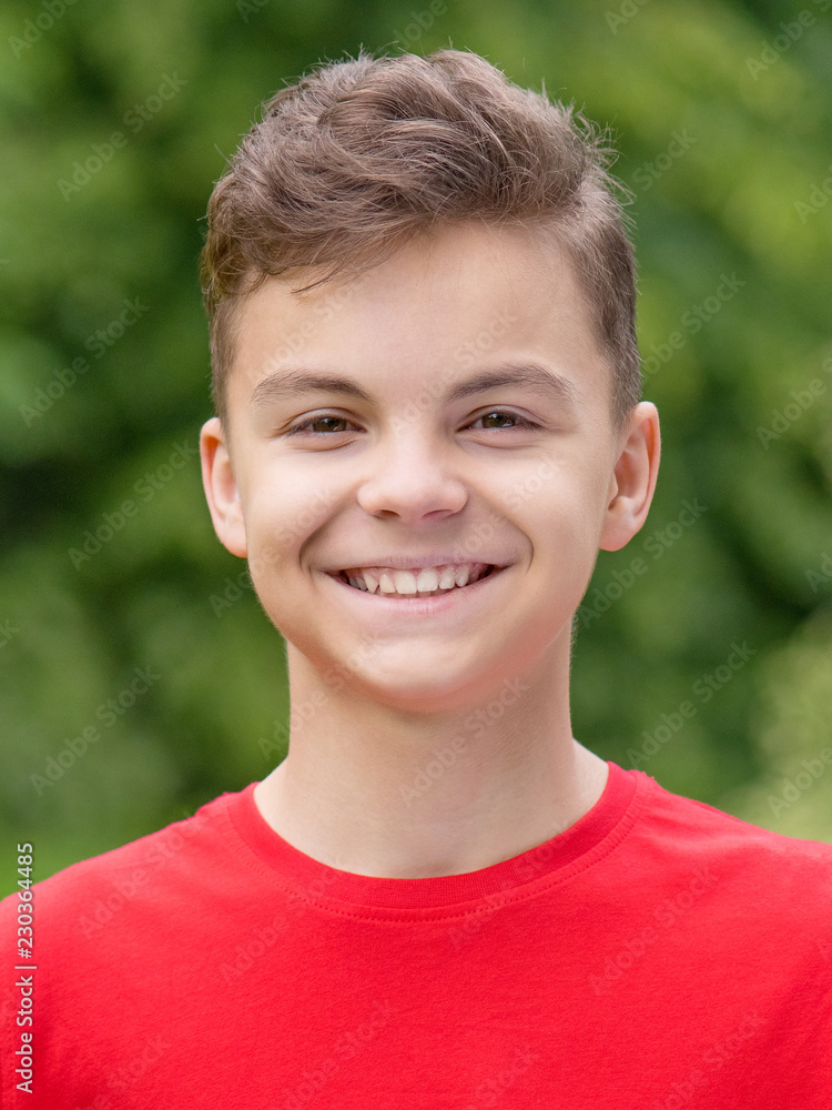 Close up emotional portrait of caucasian smiling teen boy. Head shot of handsome guy. Funny cute teenager in summer park at day. Child wearing red t-shirt looking at camera. Close up emotional portrait of caucasian smiling teen boy. Head shot of handsome guy. Funny cute teenager in summer park at day. Child wearing red t-shirt looking at camera.