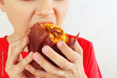 Little smiling boy is tasting the muffin on a white background close up