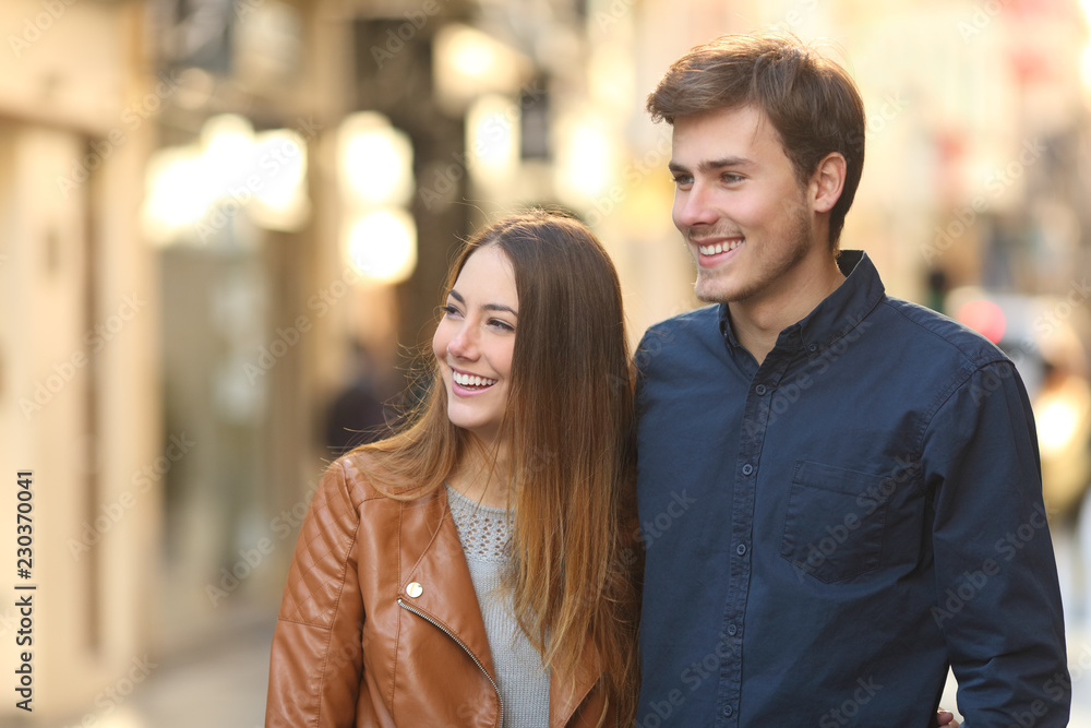 Happy couple dating walking in the street looking at side Happy couple dating walking in the street looking at side
