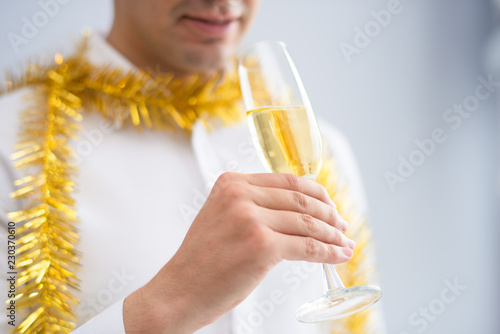 Closeup of man wearing tinsel and drinking champagne. Person celebrating Christmas. Christmas party concept. Isolated cropped view on grey background. photo