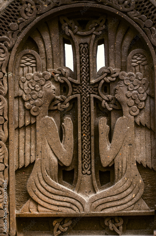 Two praying angels near the cross with intertwining ornament,engraved on dark volcanic stone