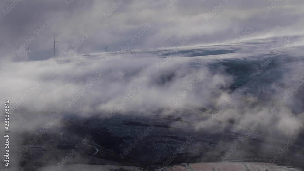 low clouds drifting besides mountains during sunrise, showing windmills in the scotland low clouds drifting besides mountains during sunrise, showing windmills in the scotland