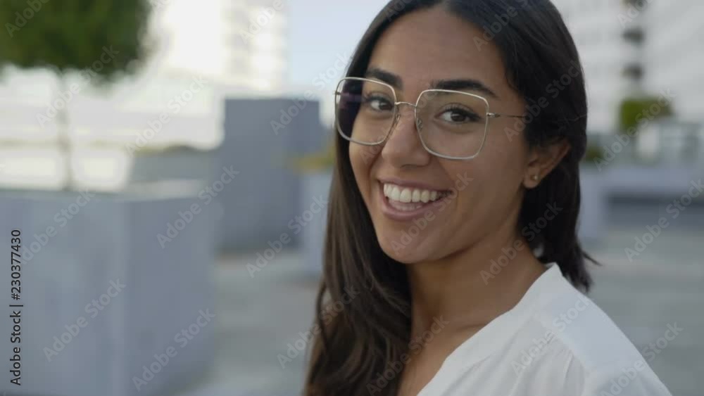 Happy Latin woman telling something and looking at camera. Beautiful smiling woman in eyeglasses talking on street. Conversation concept Happy Latin woman telling something and looking at camera. Beautiful smiling woman in eyeglasses talking on street. Conversation concept
