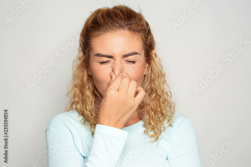 Portrait of beautiful young woman pinching nose on light background