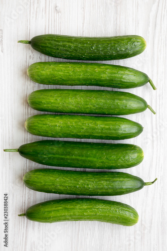 Raw organic green cucumbers on white wooden background, overhead view. Flat lay, from above, top view.