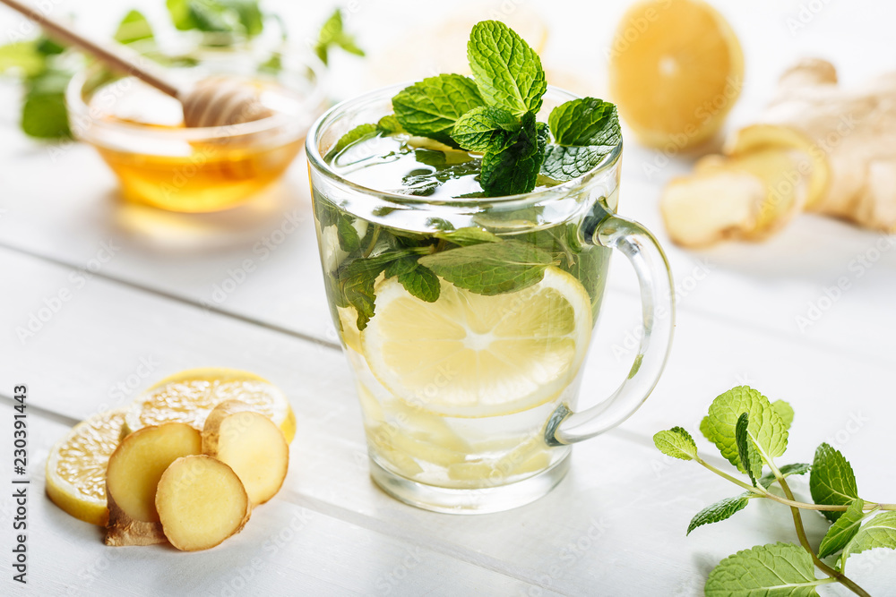 Ginger green tea in a glass for flu cold winter days. Side view on white wooden background decorated with mint, lemon and honey Ginger green tea in a glass for flu cold winter days. Side view on white wooden background decorated with mint, lemon and honey