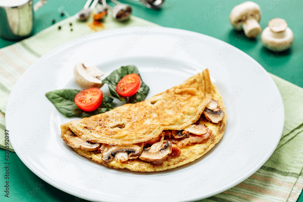 Omelet with mushrooms served on white plate with cherry tomatoes and spinach