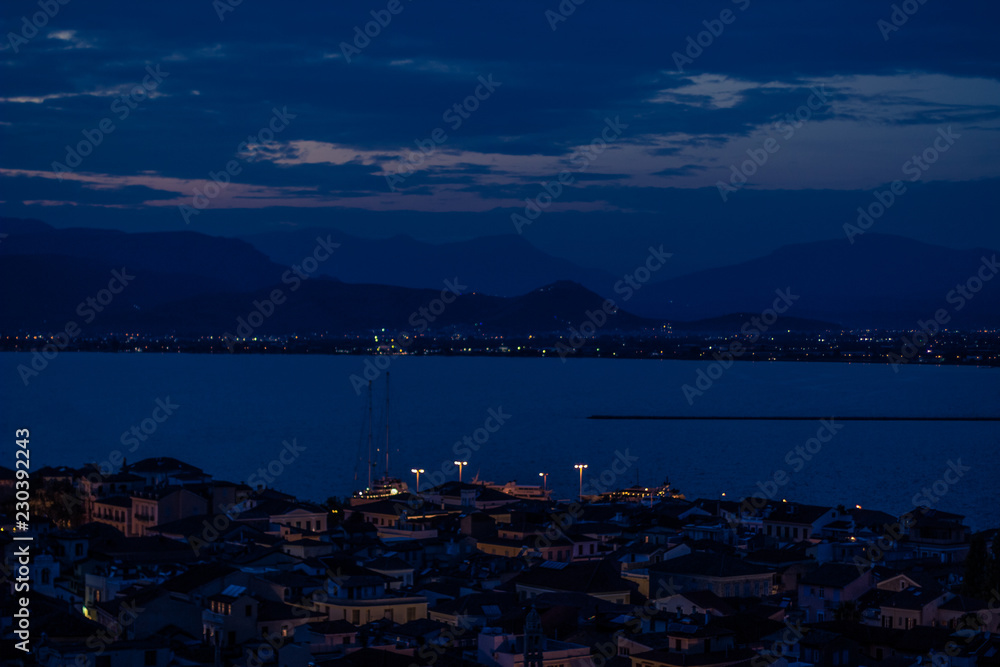 night long exposure photography of soft focus small old city street with little lantern illumination, sea front and mountain on horizon background