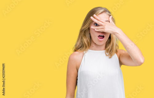 Beautiful young elegant woman over isolated background peeking in shock covering face and eyes with hand, looking through fingers with embarrassed expression.
