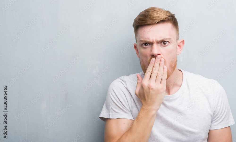 Young redhead man over grey grunge wall cover mouth with hand shocked with shame for mistake, expression of fear, scared in silence, secret concept Young redhead man over grey grunge wall cover mouth with hand shocked with shame for mistake, expression of fear, scared in silence, secret concept