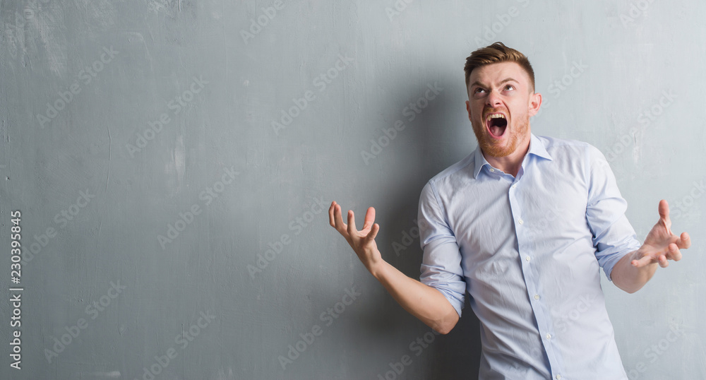 Young redhead business man over grey grunge wall crazy and mad shouting and yelling with aggressive expression and arms raised. Frustration concept. Young redhead business man over grey grunge wall crazy and mad shouting and yelling with aggressive expression and arms raised. Frustration concept.