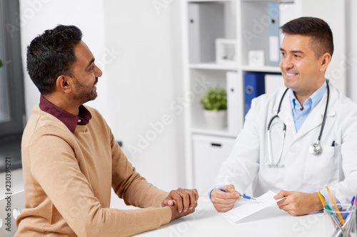 medicine, healthcare and people concept - happy doctor showing prescription to male patient at clinic