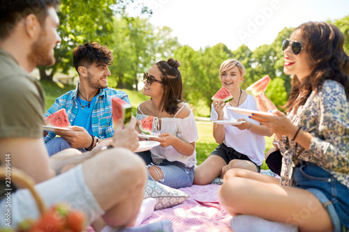 friendship, leisure and food concept - group of happy friends eating watermelon at picnic in summer park