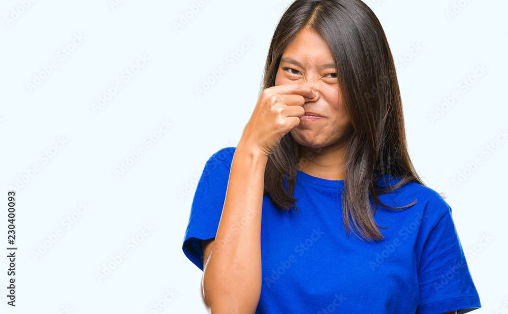 Young asian woman over isolated background smelling something stinky and disgusting, intolerable smell, holding breath with fingers on nose. Bad smells concept.