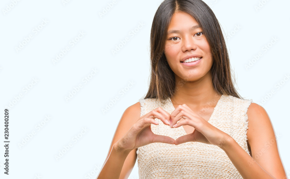 Young asian woman over isolated background smiling in love showing heart symbol and shape with hands. Romantic concept. Young asian woman over isolated background smiling in love showing heart symbol and shape with hands. Romantic concept.