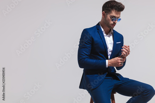 elegant man in sunglasses is sitting and touching his hands