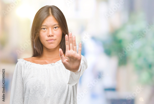 Young asian woman over isolated background doing stop sing with palm of the hand. Warning expression with negative and serious gesture on the face.