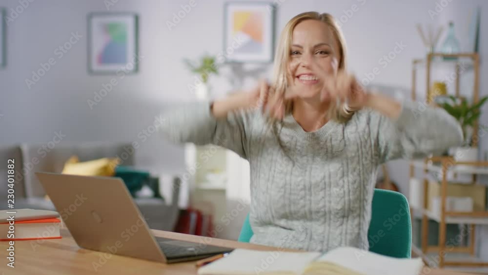 Beautiful Cheerful Blonde Does Funny Dance Routine while Sitting at Her Desk in the Living Room. Happy Woman Doing Celebratory Dancing. Beautiful Cheerful Blonde Does Funny Dance Routine while Sitting at Her Desk in the Living Room. Happy Woman Doing Celebratory Dancing.