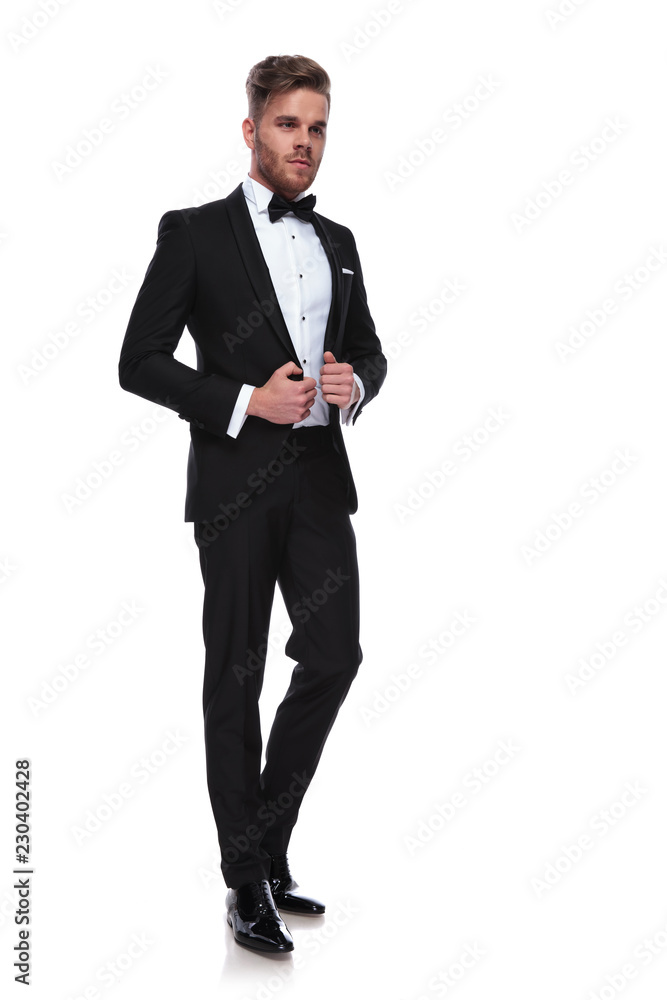 young elegant man puliing his tuxdo's collars while looking away young elegant man puliing his tuxdo's collars while looking away