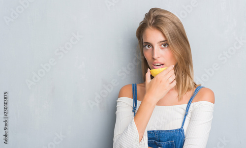 Beautiful young woman over grunge grey wall holding a lemon slice with a confident expression on smart face thinking serious