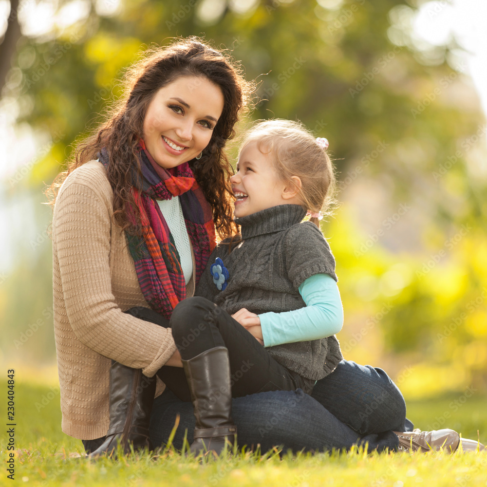Mother and daughter walking in the autumn park. Beauty nature scene with colorful background, yellow trees and leaves at fall season. Autumn outdoor lifestyle. Happy family relax on green grass Mother and daughter walking in the autumn park. Beauty nature scene with colorful background, yellow trees and leaves at fall season. Autumn outdoor lifestyle. Happy family relax on green grass