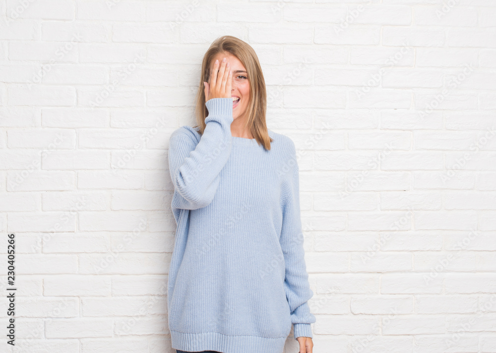 Beautiful young woman over white brick wall covering one eye with hand with confident smile on face and surprise emotion. Beautiful young woman over white brick wall covering one eye with hand with confident smile on face and surprise emotion.