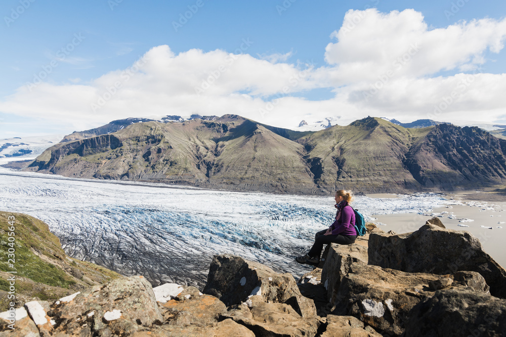 Woman sitting on rocks overlooking Skaftafellsjokull part of Vatnajokull glacier in Skaftafell national park, Iceland