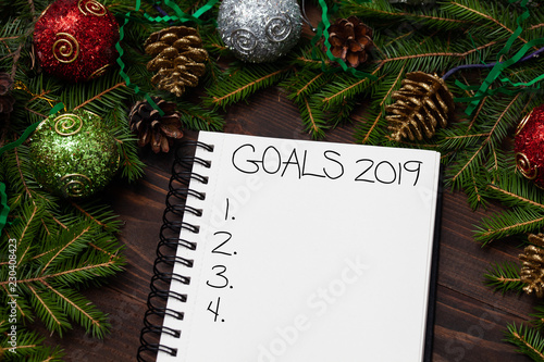 Blank notepad on wooden brown background for planning goals for the new year 2019. Christmas fir branches with New Year's toys and balls. Empty space for writing text. Top view. photo