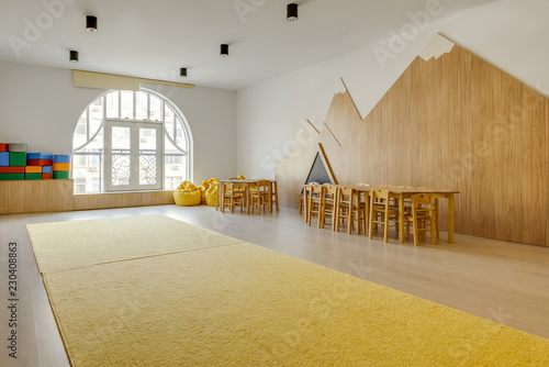 Canvastavla playing room interior with wooden chairs and tables, yellow carpet, bean bag cha