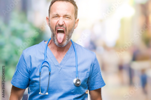 Middle age hoary senior doctor man wearing medical uniform over isolated background sticking tongue out happy with funny expression. Emotion concept.