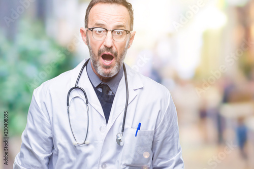 Middle age senior hoary doctor man wearing medical uniform isolated background afraid and shocked with surprise expression, fear and excited face.