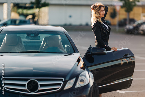 Photo of young blonde woman at open door of black car © snedorez