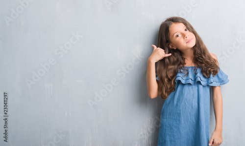 Young hispanic kid over grunge grey wall smiling doing phone gesture with hand and fingers like talking on the telephone. Communicating concepts.