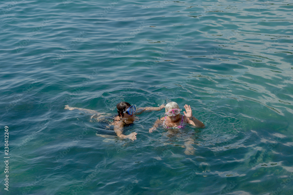 Two women are swimming in clear water of sea.